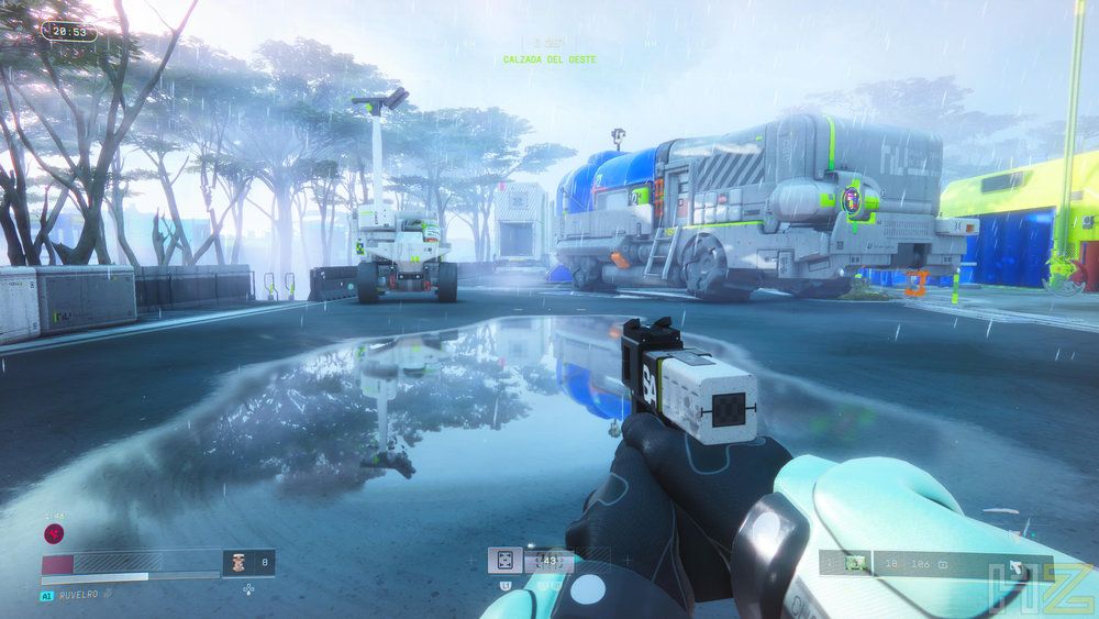 Vista en primera persona de un personaje empuñando un arma en un escenario futurista con un charco en el suelo que refleja el entorno y estructuras industriales al fondo.