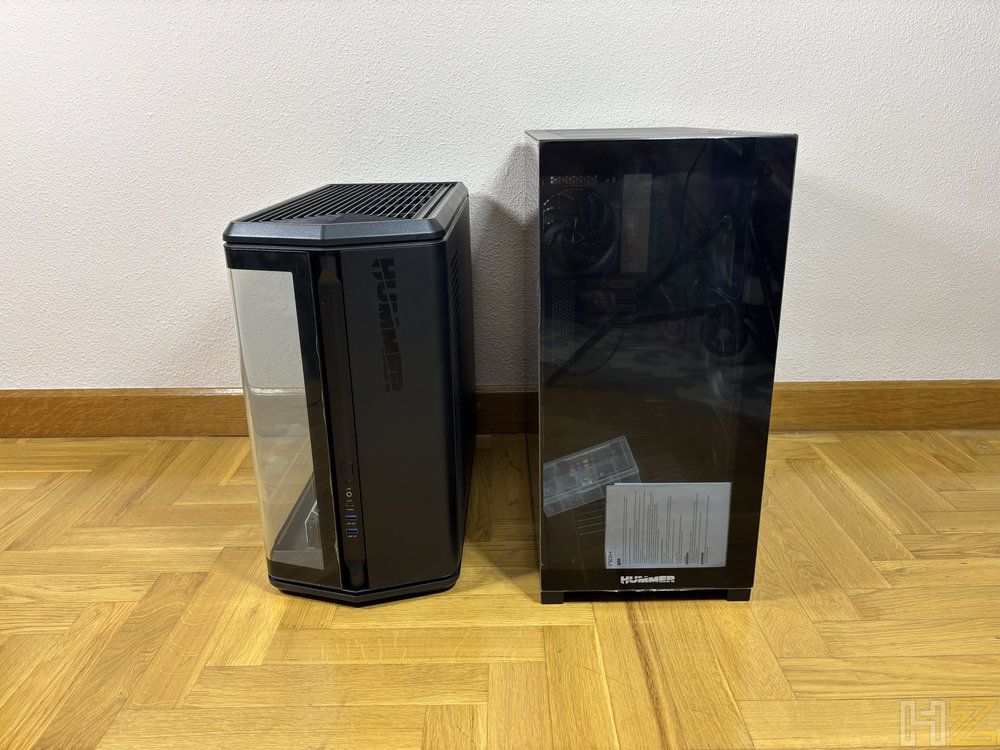 Comparativa de tamaño entre el chasis Nox Hummer Anvil y una torre de PC convencional sobre un suelo de madera.