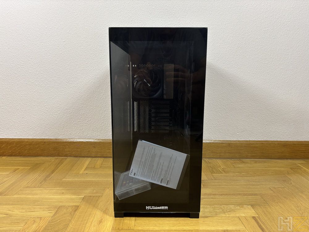 Vista frontal de la torre de ordenador Nox Hummer Blade con panel de cristal templado oscuro sobre un suelo de parqué.