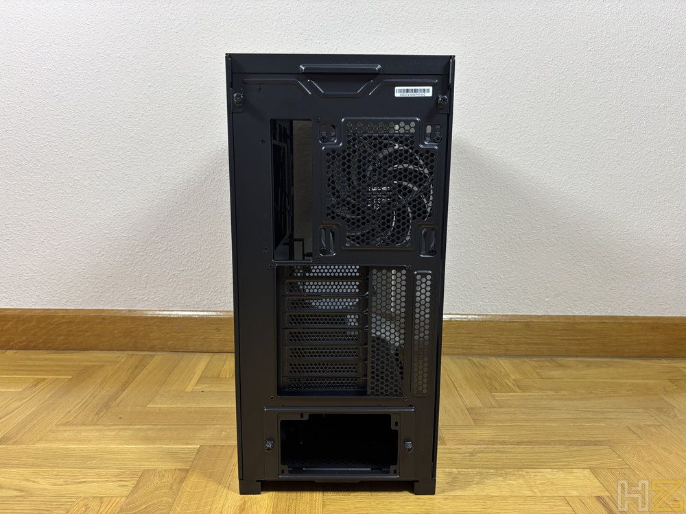 Panel posterior de una torre de ordenador negra que muestra el hueco para la fuente de alimentación, ranuras de expansión y rejilla del ventilador trasero.