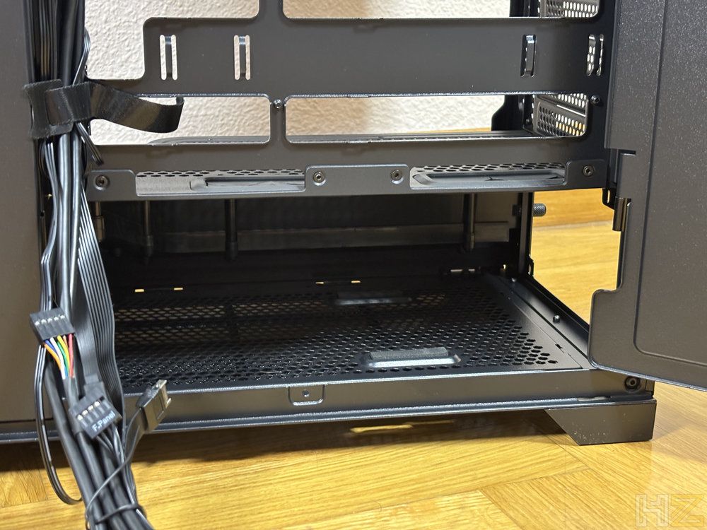 Vista detallada del compartimento inferior de una caja de PC negra con rejilla de ventilación y cableado lateral organizado.