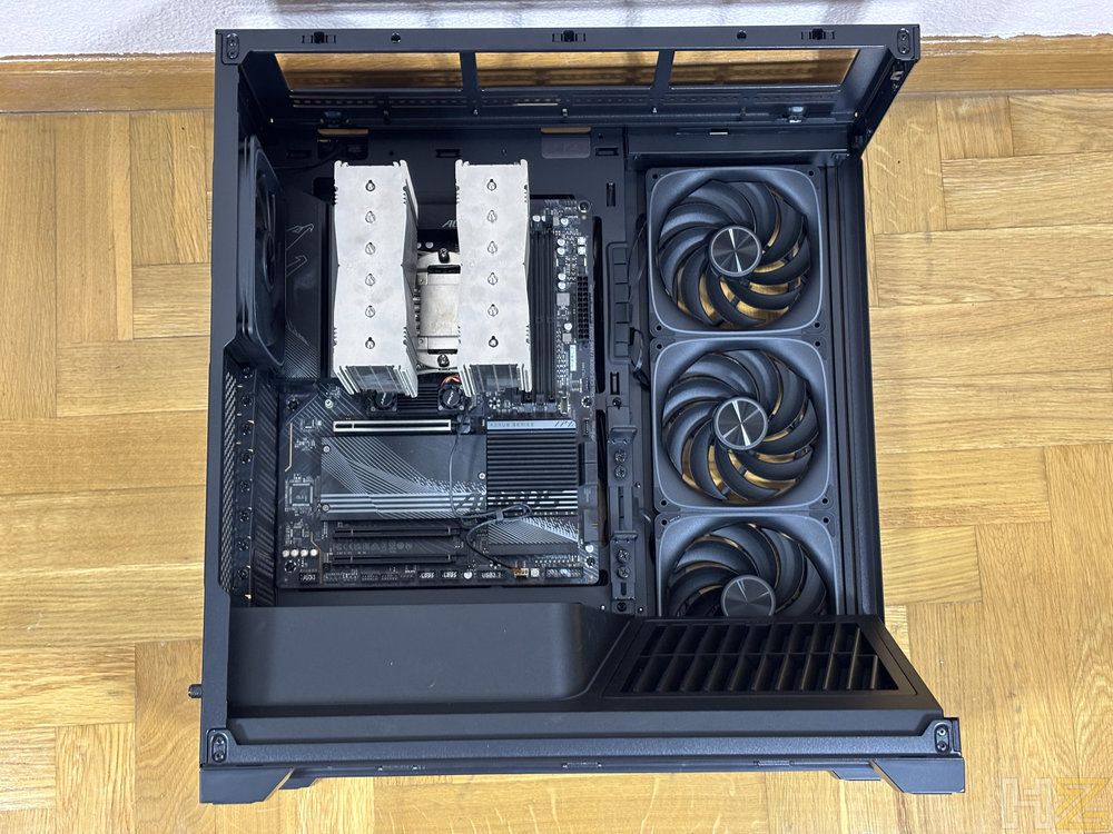 Vista interior de una caja de PC Nox Hummer Blade con placa base instalada, disipador de CPU de doble torre y tres ventiladores frontales negros sobre suelo de parqué.