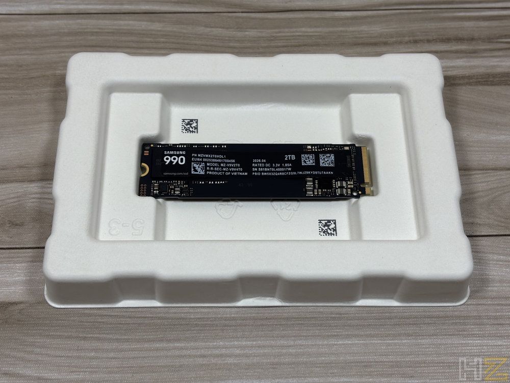 Unidad de estado sólido Samsung 990 Pro de 2 TB dentro de su soporte protector de cartón blanco reciclable sobre una mesa de madera.