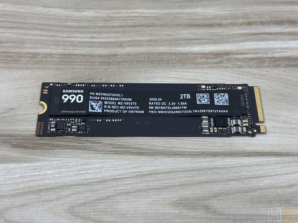 Unidad de almacenamiento SSD Samsung 990 de 2TB en formato NVMe M.2 sobre una superficie de madera clara.