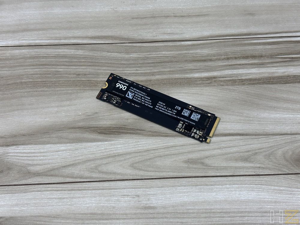 Unidad de almacenamiento SSD Samsung 990 Pro en formato M.2 dispuesta sobre una superficie de madera clara.