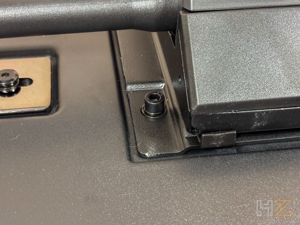 Primer plano del mecanismo de montaje inferior de una silla noblechairs AURA con tornillos Allen fijados a la base metálica negra.
