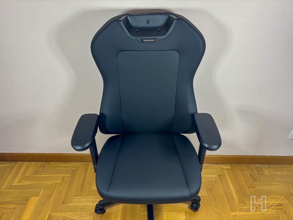 Silla gaming noblechairs AURA en color negro con acabado AtmoShell, vista frontal sobre suelo de parquet.