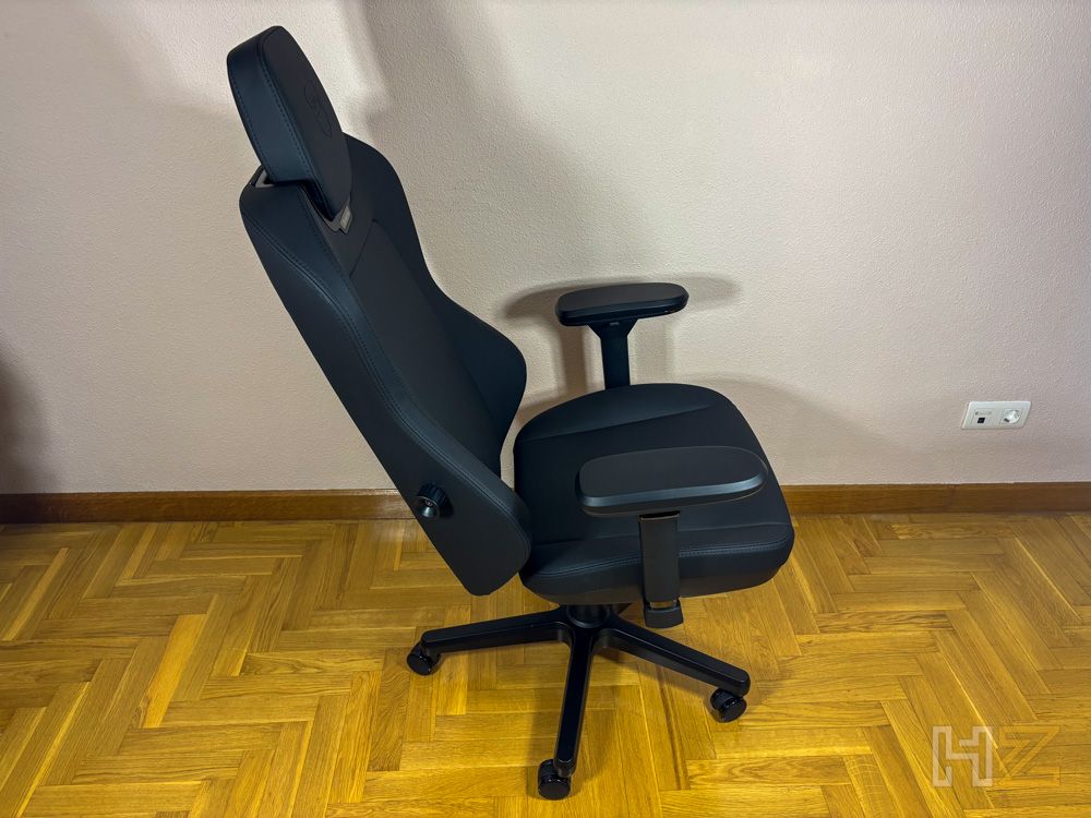 Silla ergonómica noblechairs AURA en color negro vista de perfil sobre suelo de parqué.